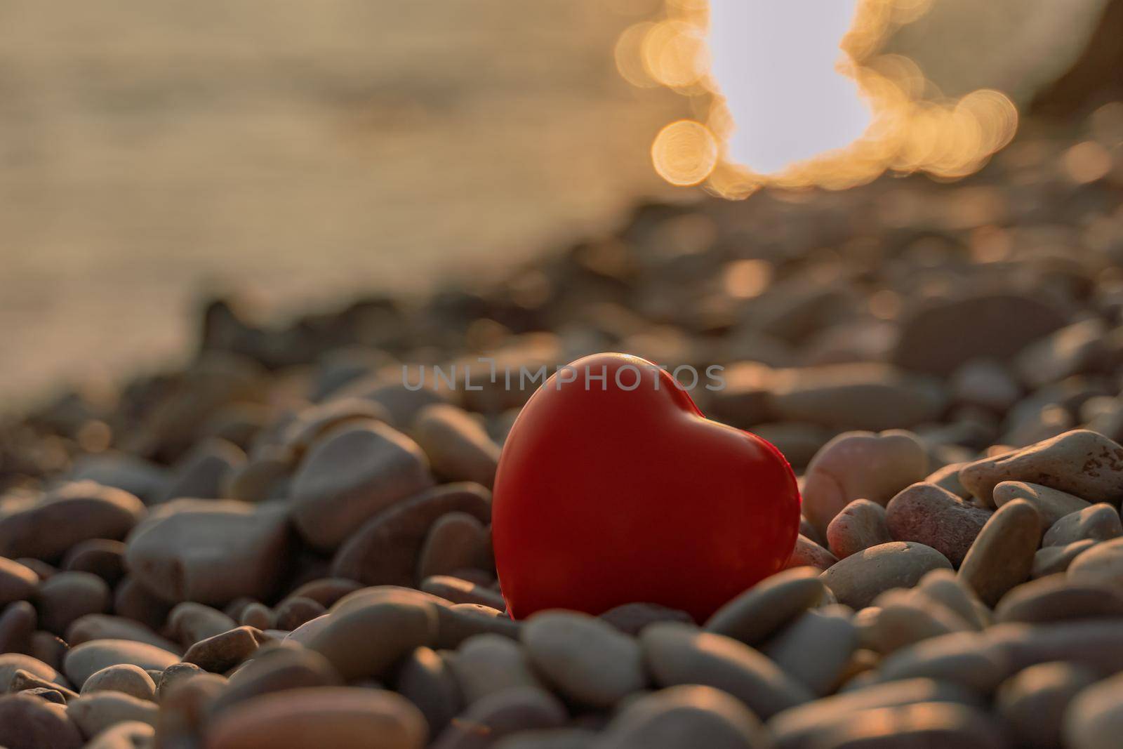 Valentine's Day concept. Red heart romantic love symbol on pebble beach at sunset with copy space. Template for inspirational compositions and postcards with quotes