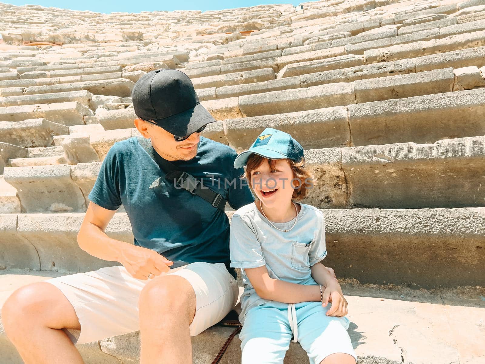 Young father dad and his school boy kid son tourists visiting ancient antique coliseum amphitheater ruins in hot summer day.