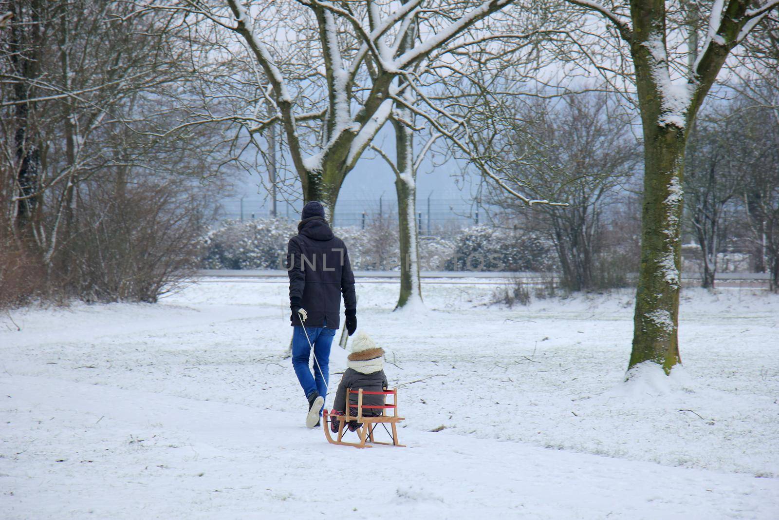 Father and son walking in the snow with a small sleigh by studioportosabbia