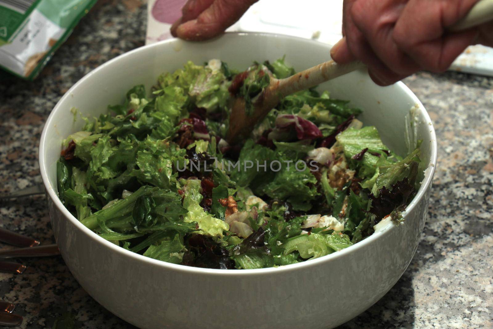 Man preparing a green salad with wallnuts, goat cheese and oil