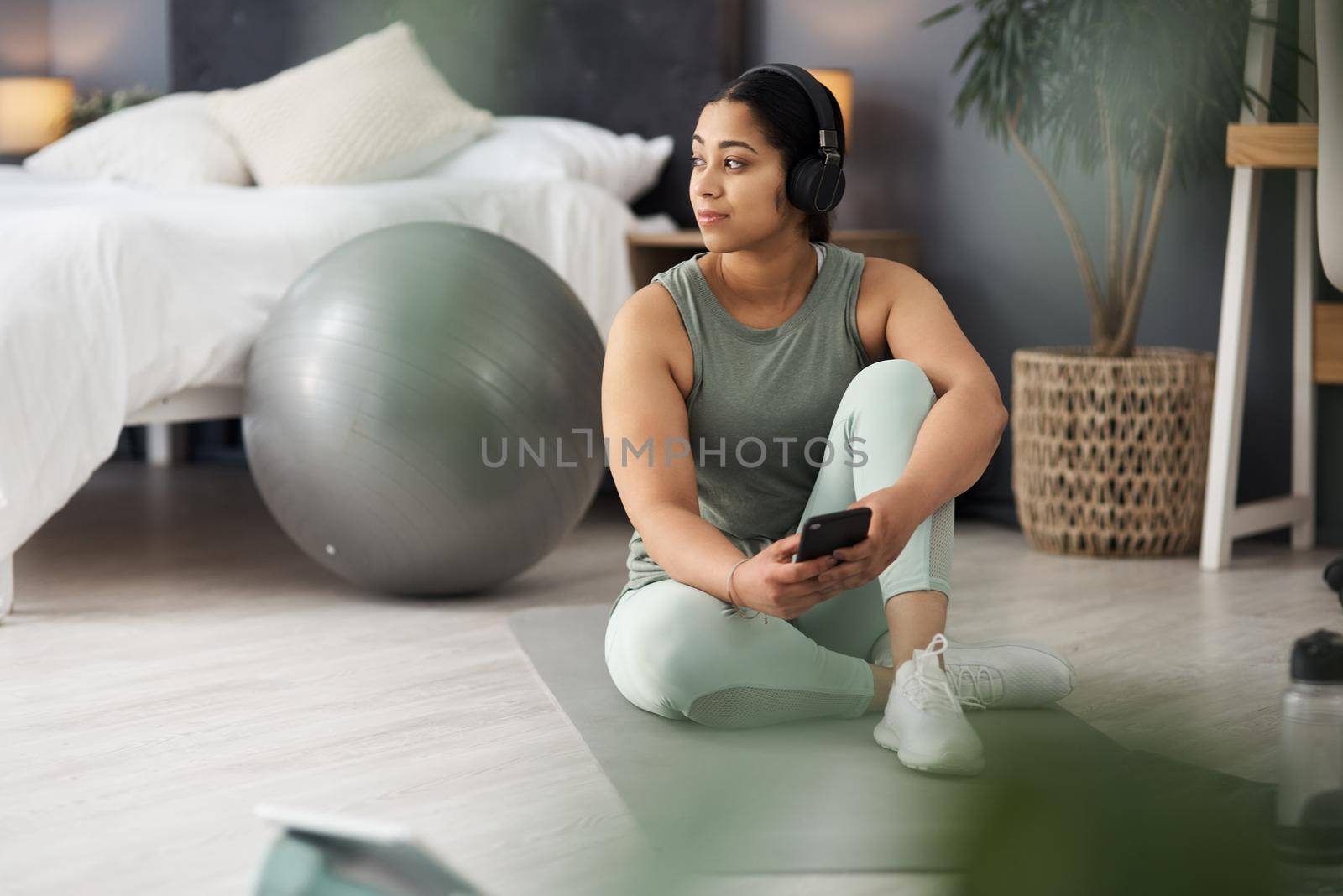 Taking breaks with her connections. a sporty young woman wearing headphones and using a cellphone while exercising at home. by YuriArcurs