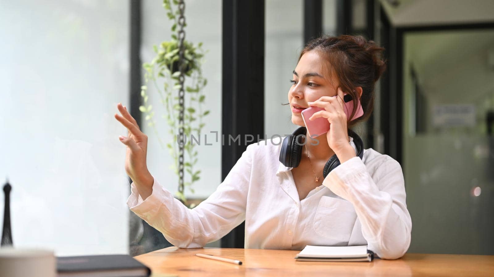 Charming young woman having talking conversation on mobile phone while sitting in coffee shop by prathanchorruangsak
