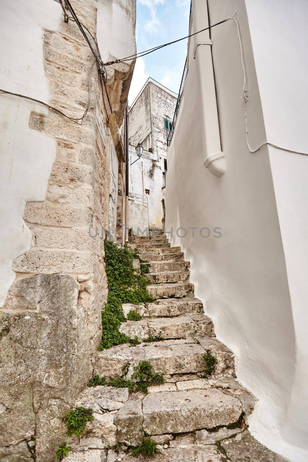 Admirable architecture of an ancient streets decorated with plants in flowerpots. Old steps leading up. Downtown, white city Ostuni, Bari, Italy. Tourism, travel concept.