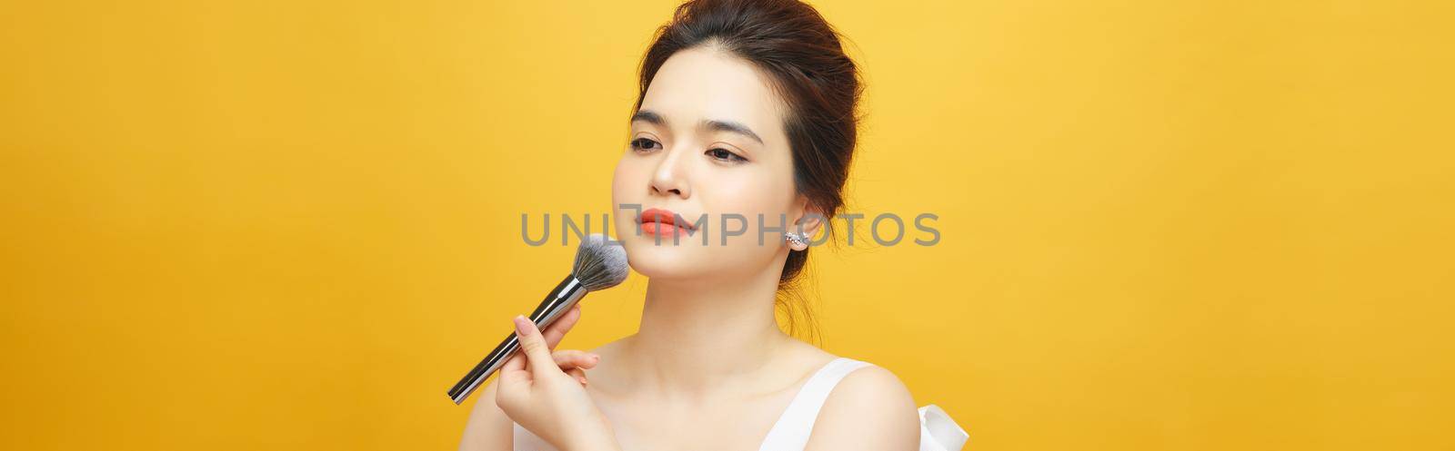 beautiful woman holding makeup brush over yellow by makidotvn