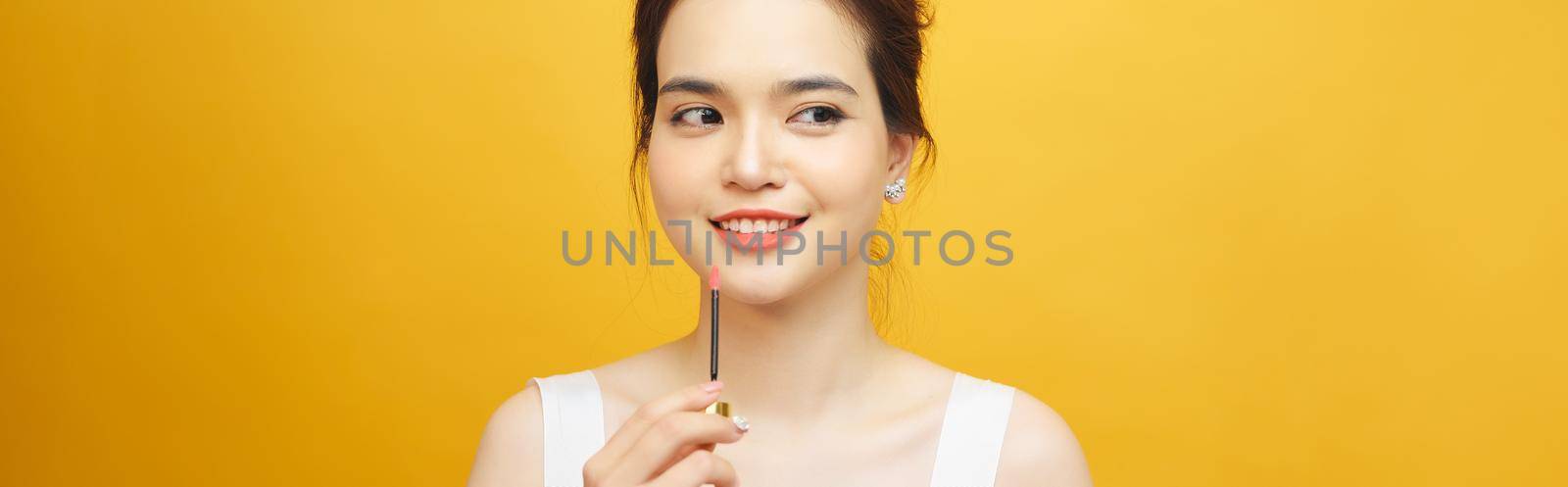 Perfect girl holding lipstick on yellow background, close up portrait.