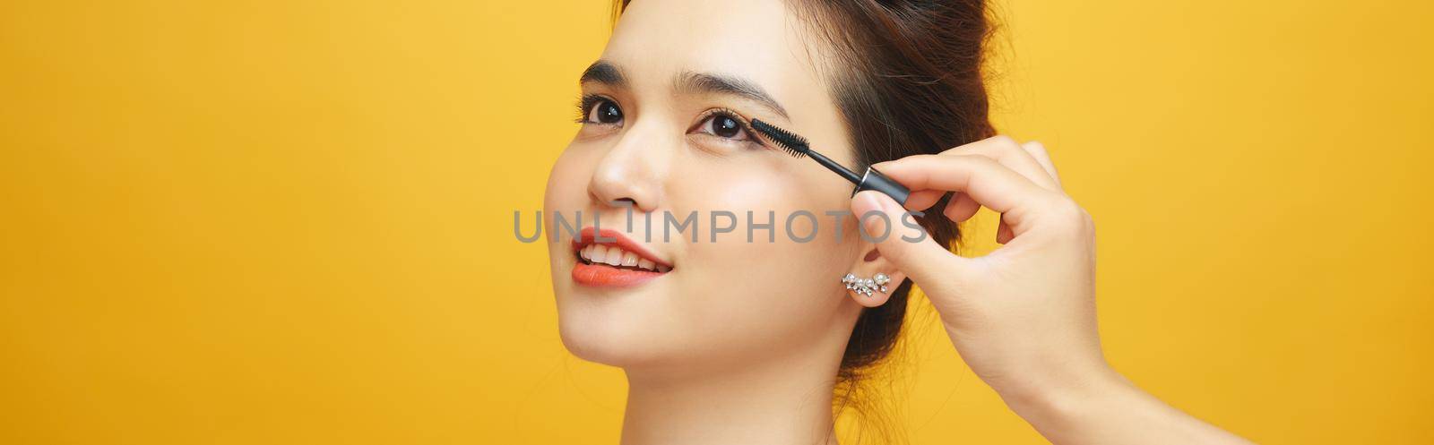 Beautiful women use mascara on a yellow background