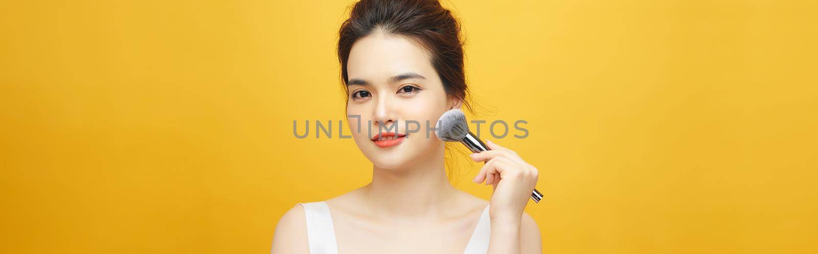 beautiful woman holding makeup brush over yellow