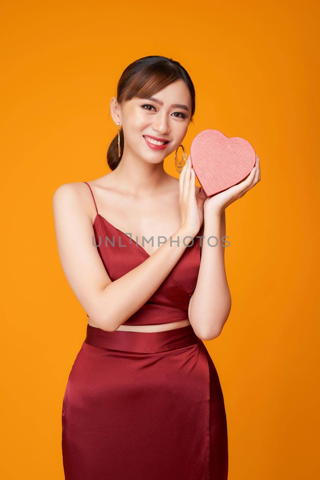 Beautiful woman with heart shaped box on color background.