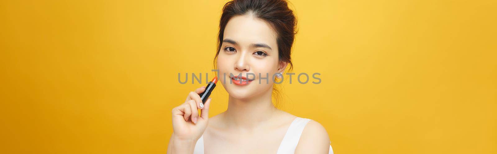 Beautiful asian woman holding red lipgloss on yellow background