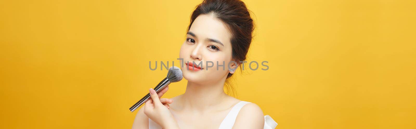 beautiful woman holding makeup brush over yellow