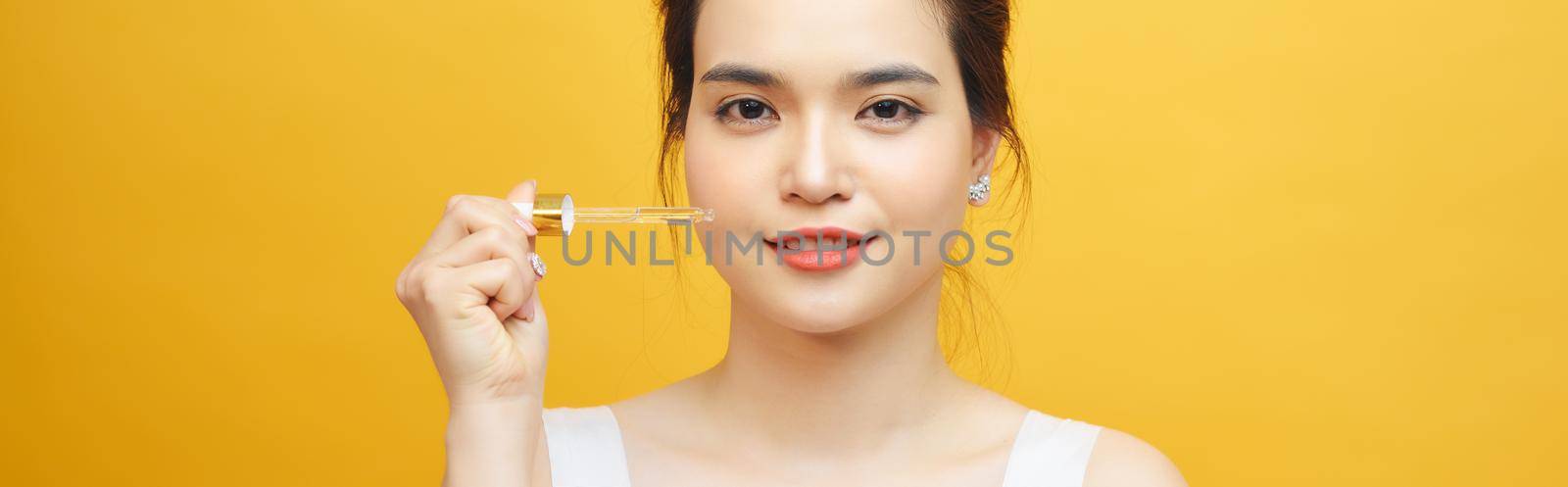 young beautiful asian woman hold pipette of serum for skin on yellow background by makidotvn
