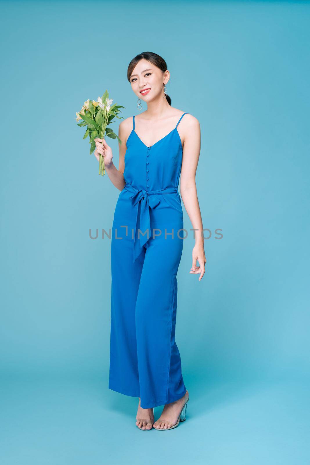 Beautiful girl in the blue dress with flowers in hands on a light background 