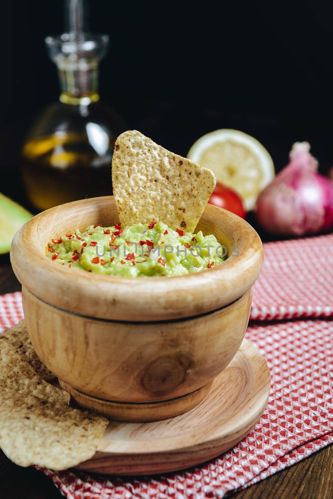 homemade guacamole in a wood bowl with nachos next to avocado and other ingredients, typical mexican healthy vegan cuisine with rustic dark food photo style