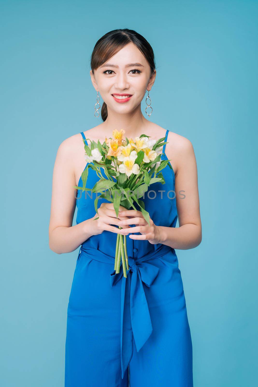 Attractive Asian woman in blue dress holding bouquet of flowers over blue background by makidotvn