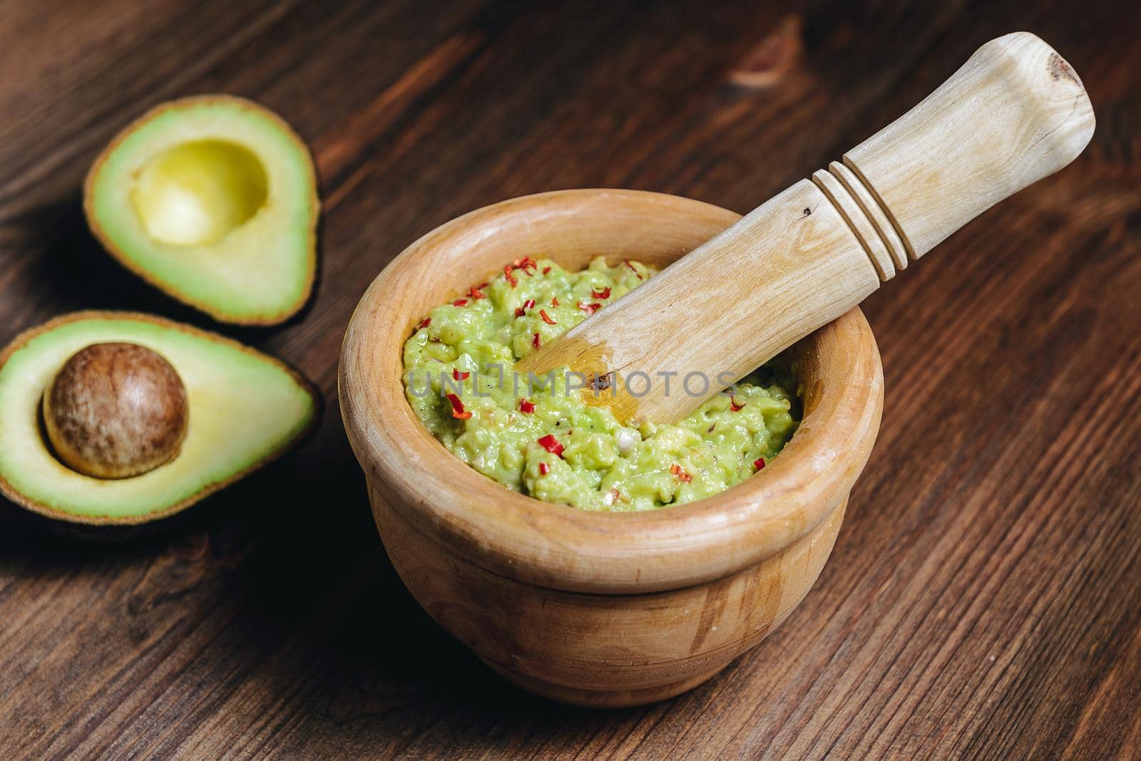 traditional guacamole in a wood bowl and cut half avocado on wooden table, typical mexican healthy vegan cuisine with rustic dark food photo style