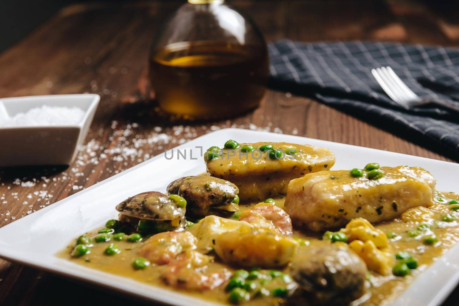 healthy traditional spanish hake dish with green seafood sauce with clams, prawns, green peas and egg, typical mediterranean cuisine with rustic dark food photo style