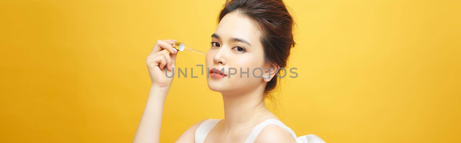 Closeup shot of cosmetic oil applying on young woman's face with pipette. Beauty therapy concept.