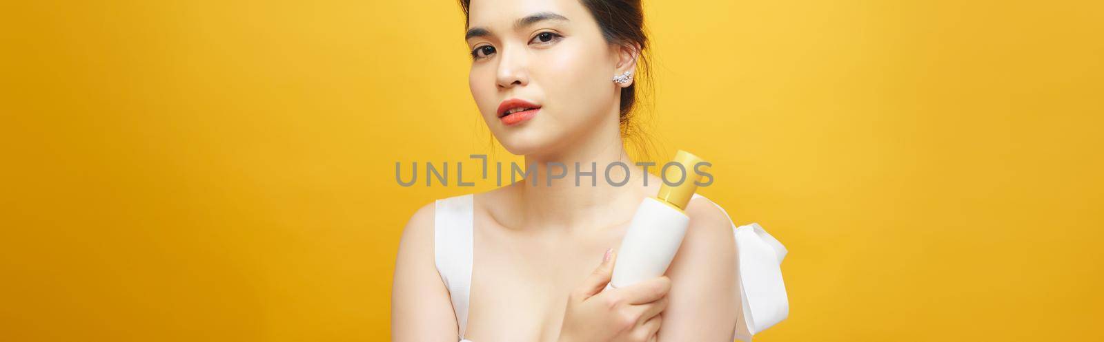 Portrait of Asian woman holding beauty product over yellow background
