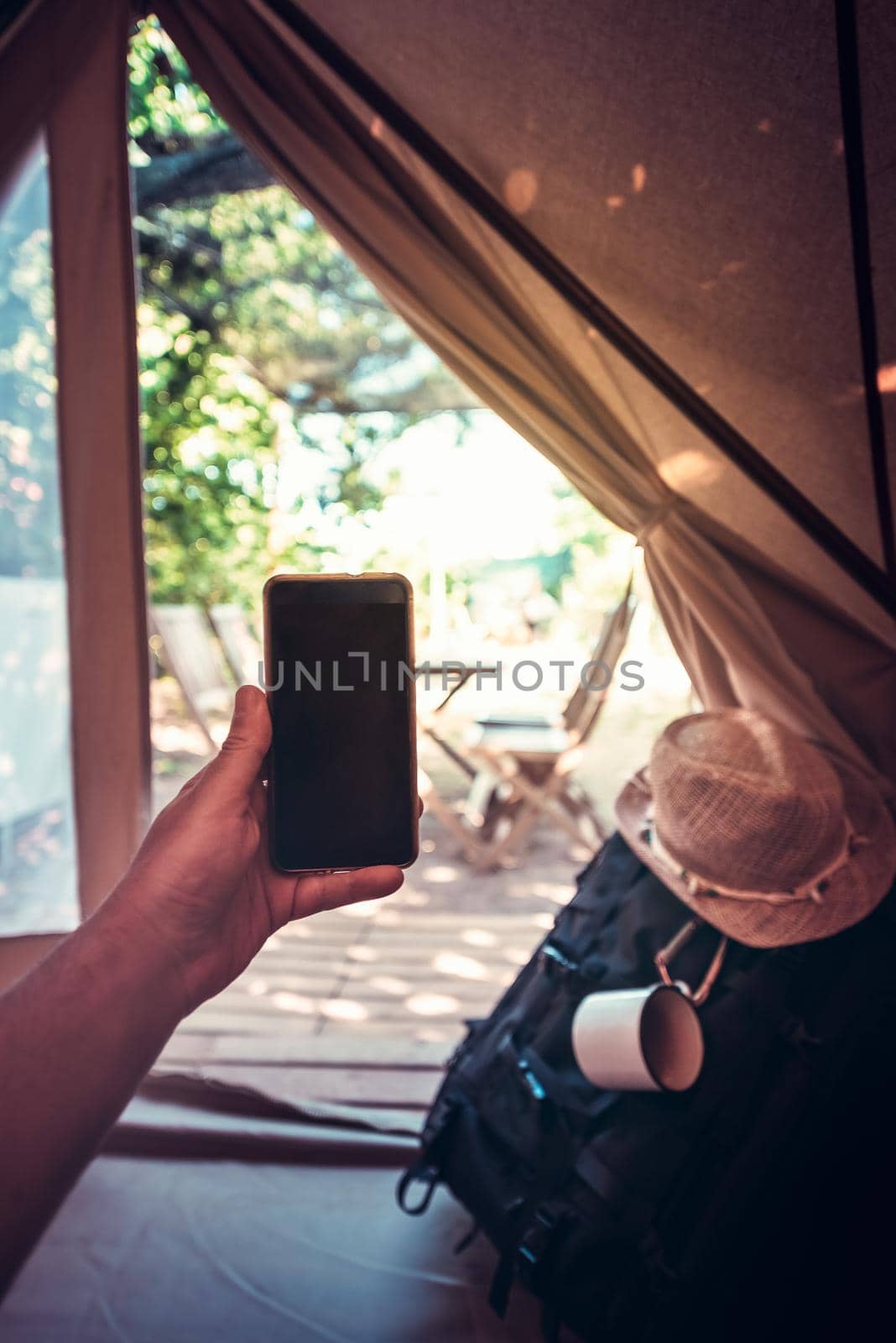vertical view of a hand of a hiker person resting while consulting the phone in a camping tent, travel discovery concept, point of view shot