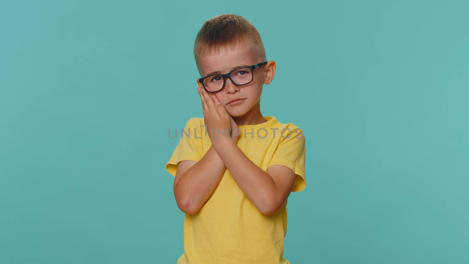 Dental problem. Little toddler children boy touching cheek, closing eyes with expression of terrible suffer from painful toothache, sensitive teeth, cavities. Young preschool kid in on blue background