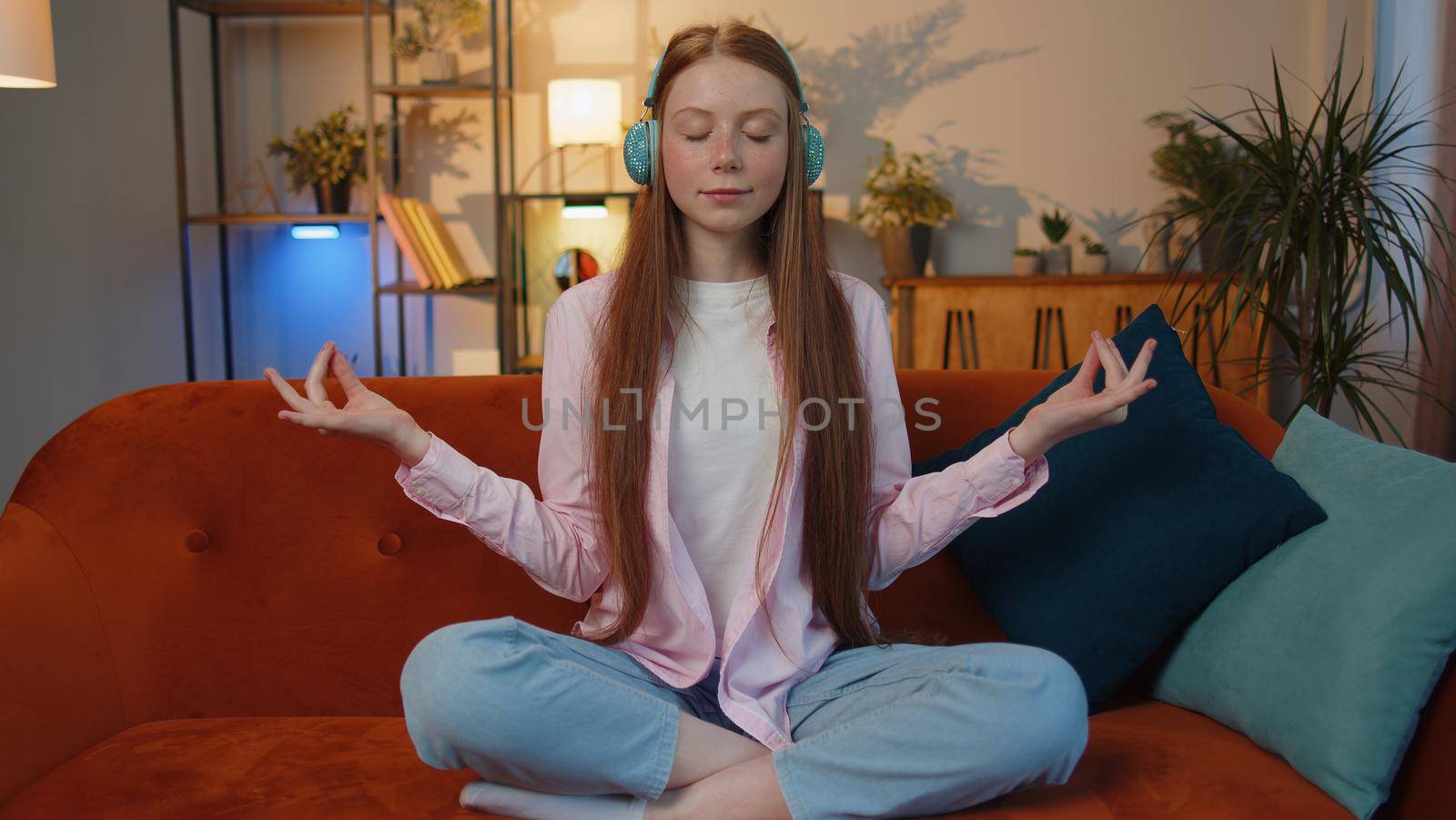 Keep calm down, relax, inner balance. Young redhead child girl breathes deeply with mudra gesture eyes closed meditating with concentrated thoughts, peaceful mind sit at home in living room on couch