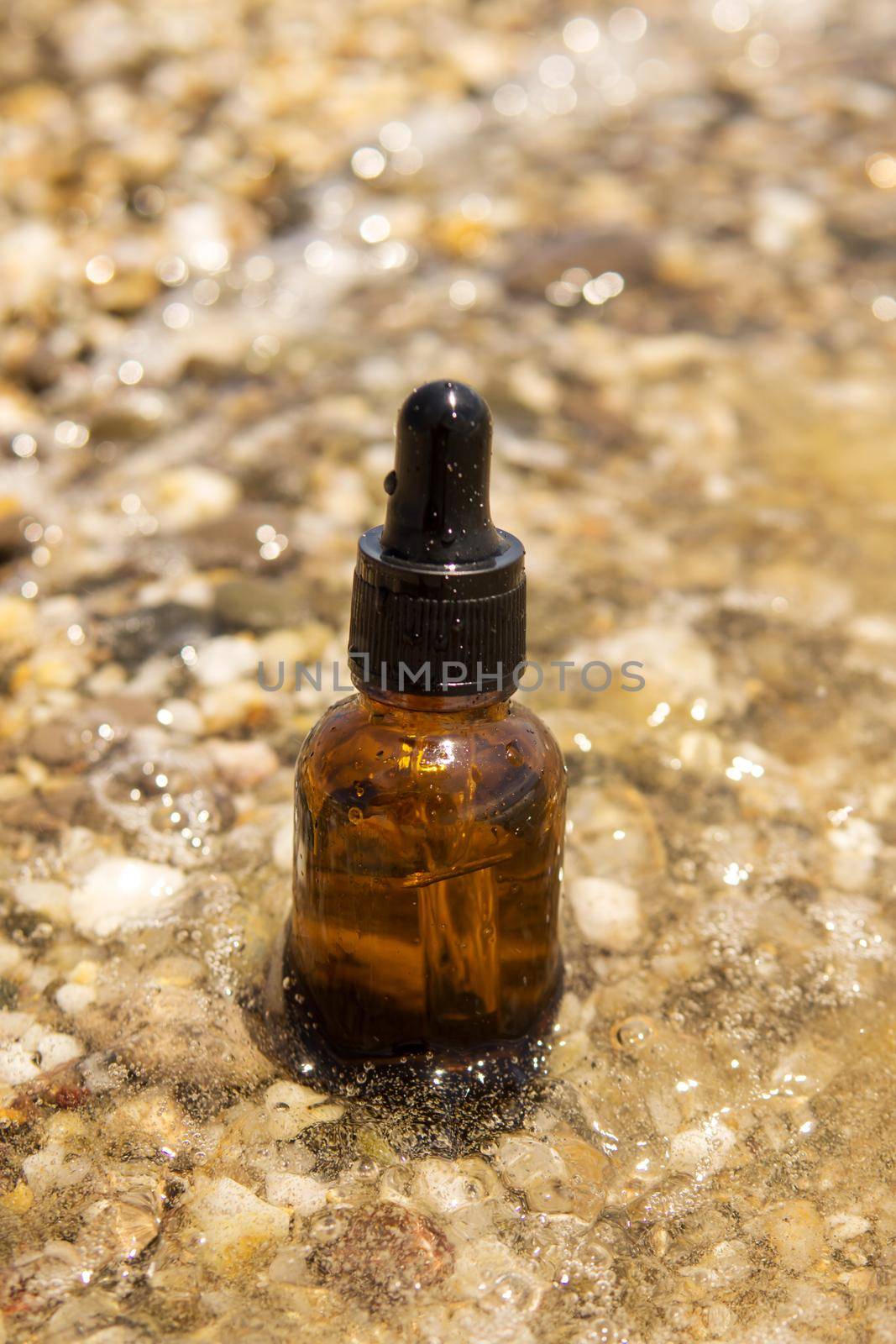 Cosmetic serum for the skin in a glass bottle. A bottle with an eyedropper on a pebble beach by the sea. Essences for skin care on the background of stones. The concept of natural cosmetics and SPA products.