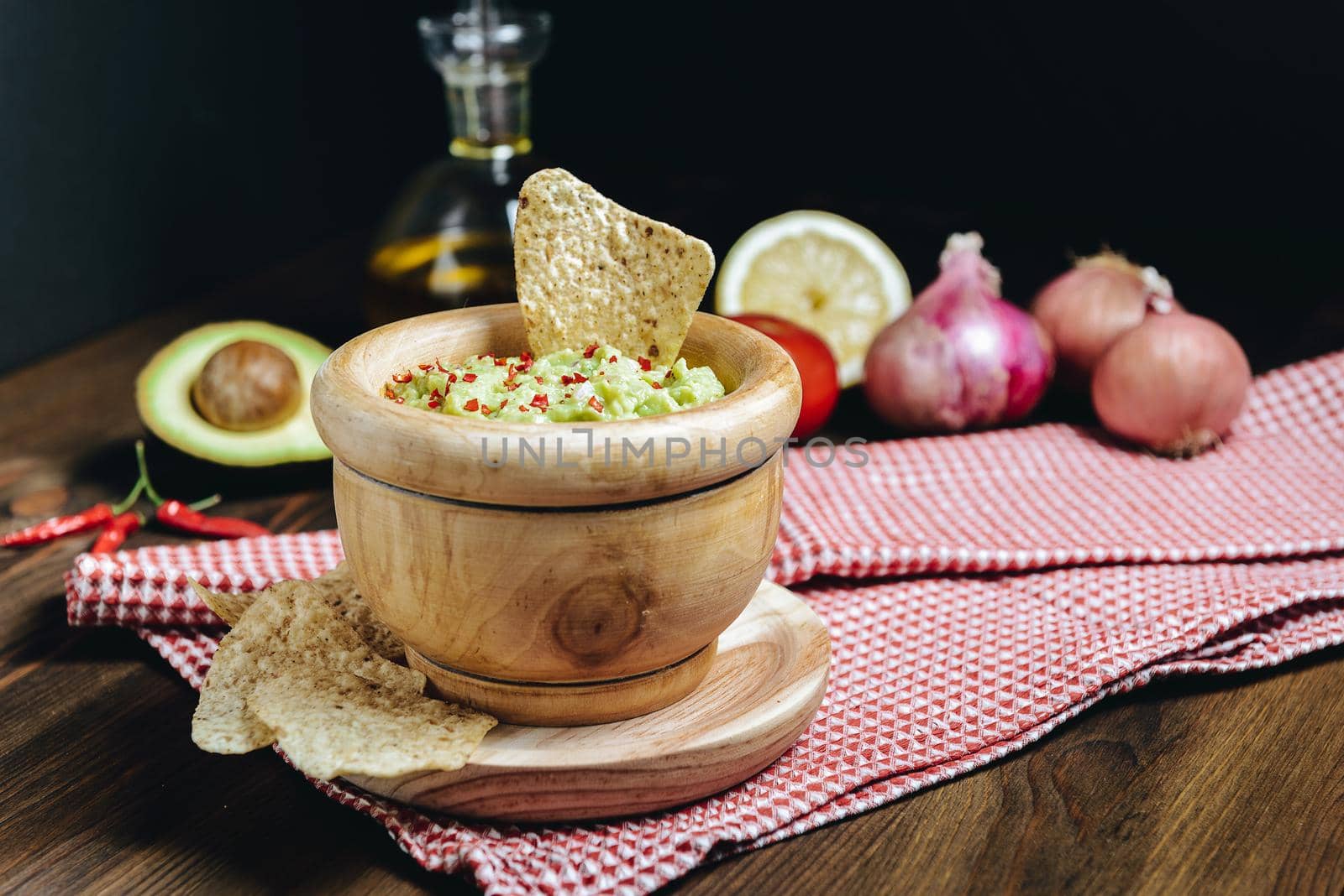 guacamole in a wood bowl with nachos next to fresh ingredients, typical mexican healthy vegan cuisine with rustic dark food photo style