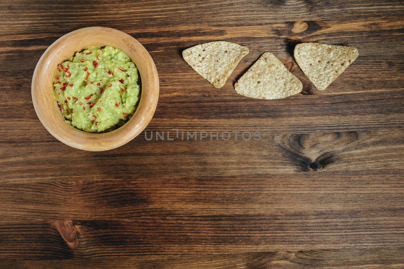 homemade guacamole with nachos in a wood bowl on a wooden table, typical mexican healthy vegan cuisine, top view and copy space for text