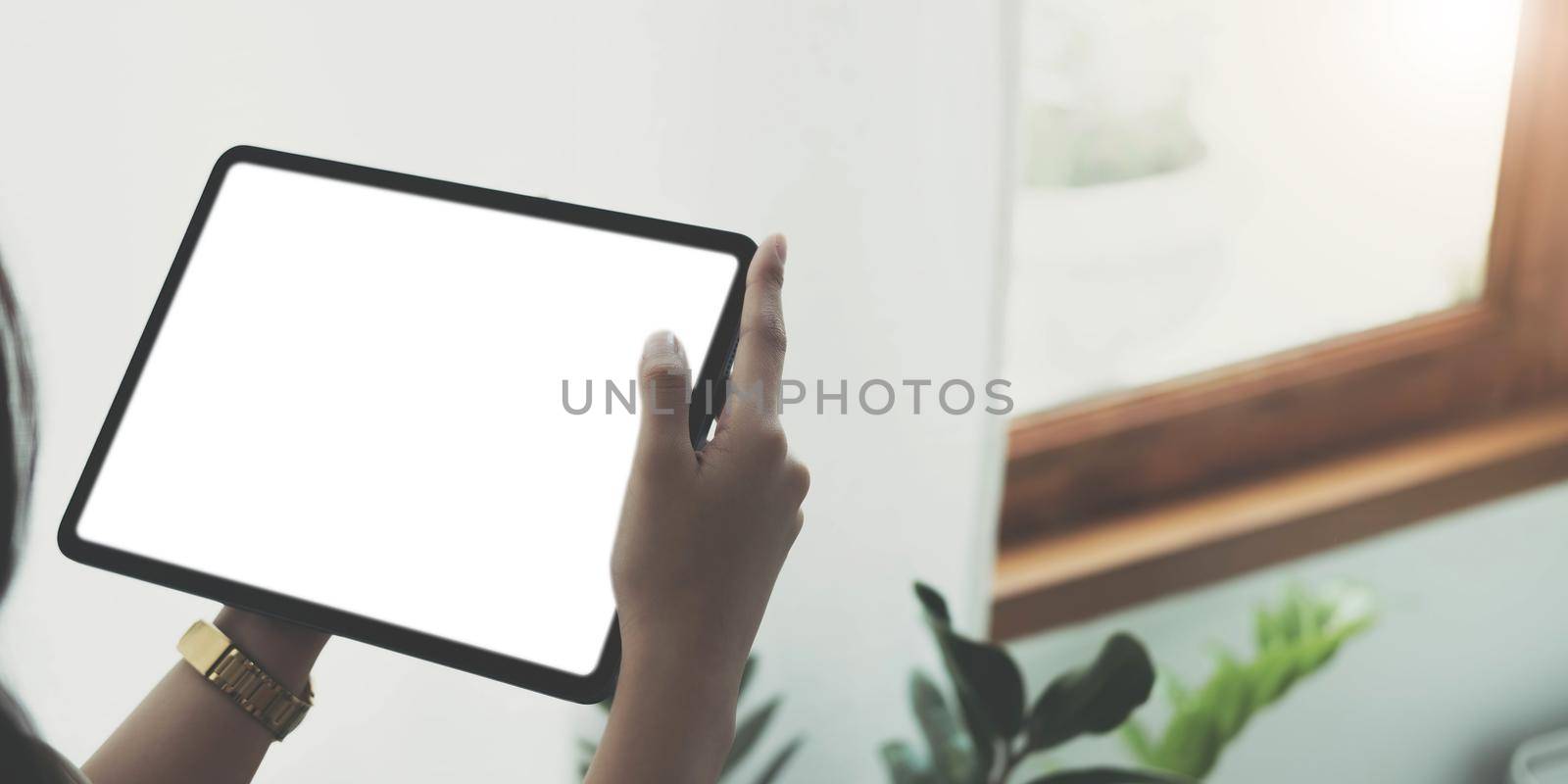 Mockup image of woman's hand holding black tablet pc with blank white screen in wooden cafe.