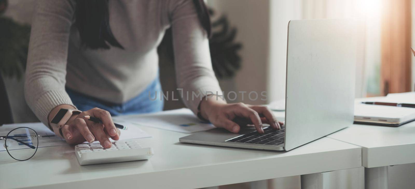 Finance Concept. Woman hold a graph pen, press a calculator and make money by writing reports, and memos, and analyzing business documents with a laptop computer vertically..