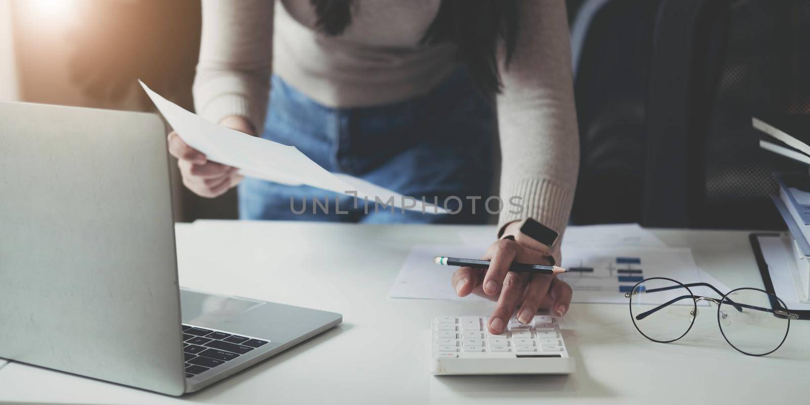 Finance Concept. Woman hold a graph pen, press a calculator and make money by writing reports, and memos, and analyzing business documents with a laptop computer vertically. by wichayada