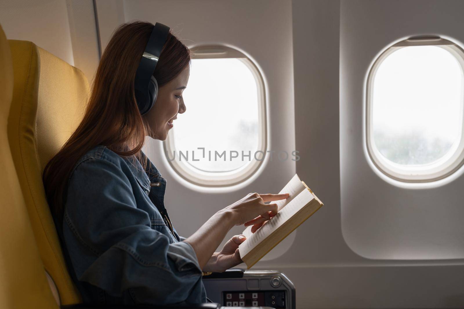 Beautiful asian travel woman reading a book in airplane by nateemee