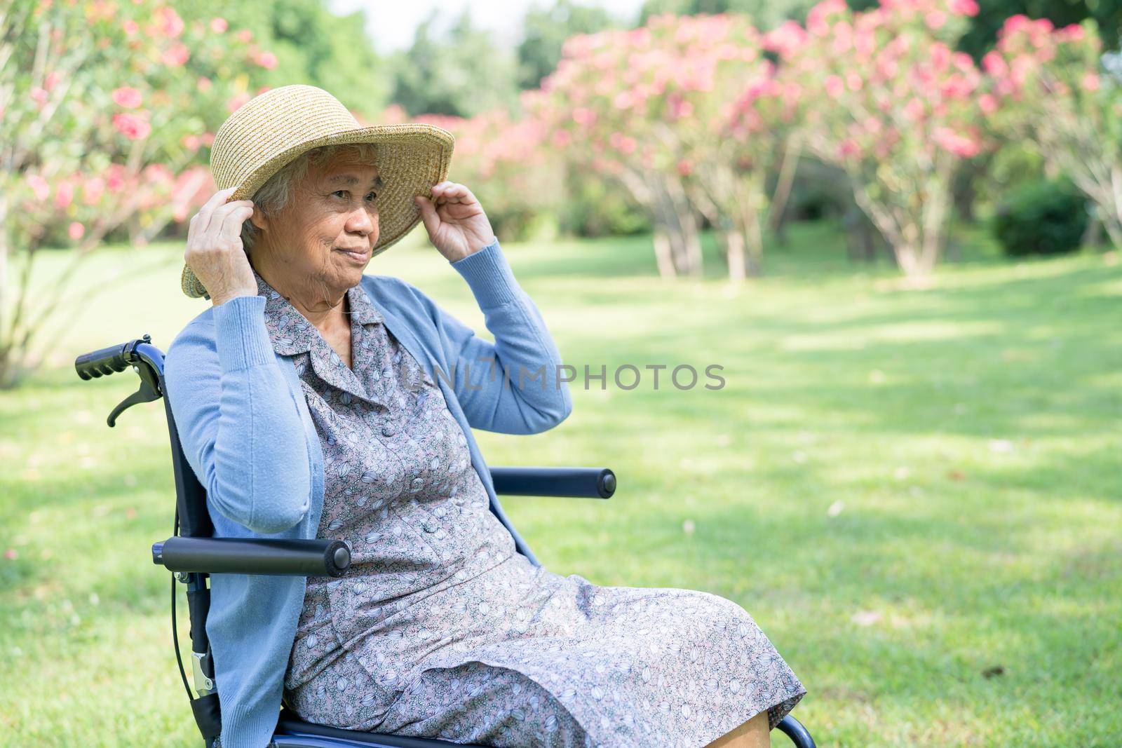 An elderly woman traveler with straw hat sitting on wheelchair for travel in park.