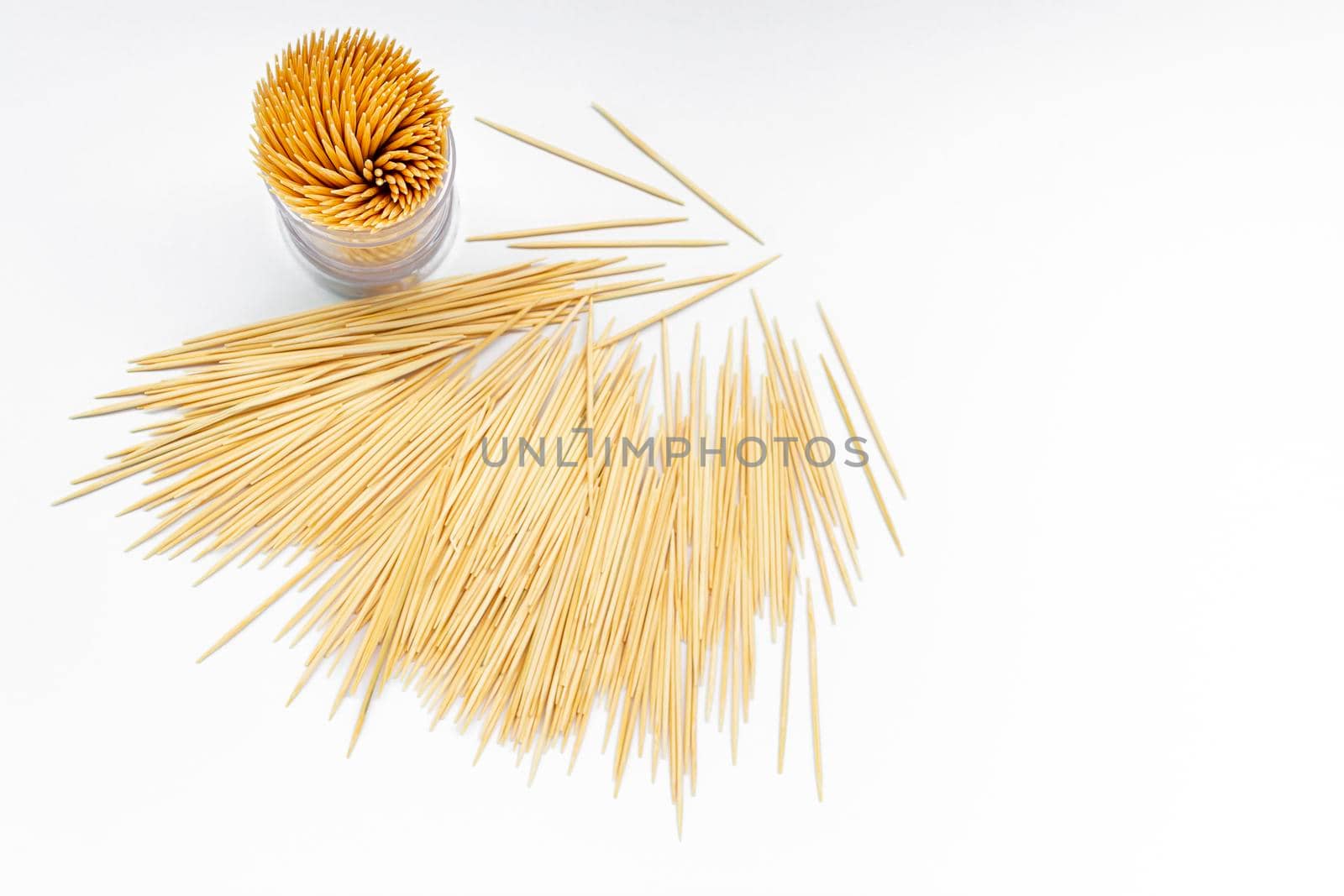 Pile of round wooden toothpicks and toothpick box with a plastic cover on white background. Copy space. Directly above. Flat lay.
