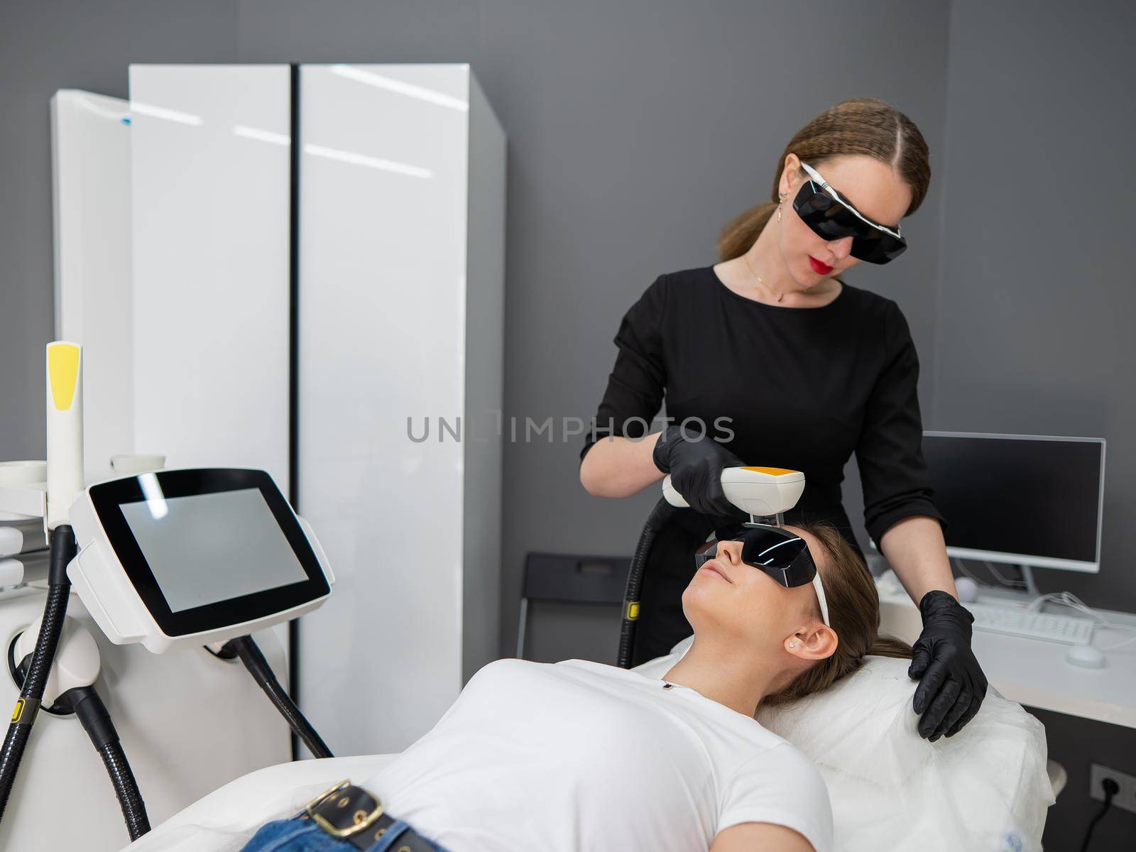 Young caucasian woman in goggles on photorejuvenation procedure. Doctor cosmetologist with a female patient. by mrwed54