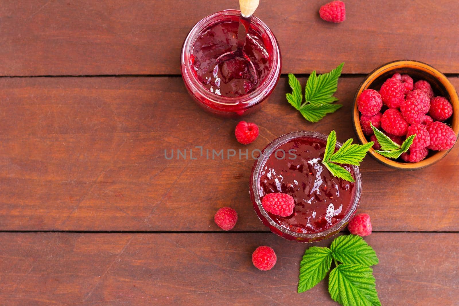 fresh raspberry jam in a glass jar on a wooden table, next to fresh raspberries. concept of homemade jam, preserves for winter, selective focus and copy space