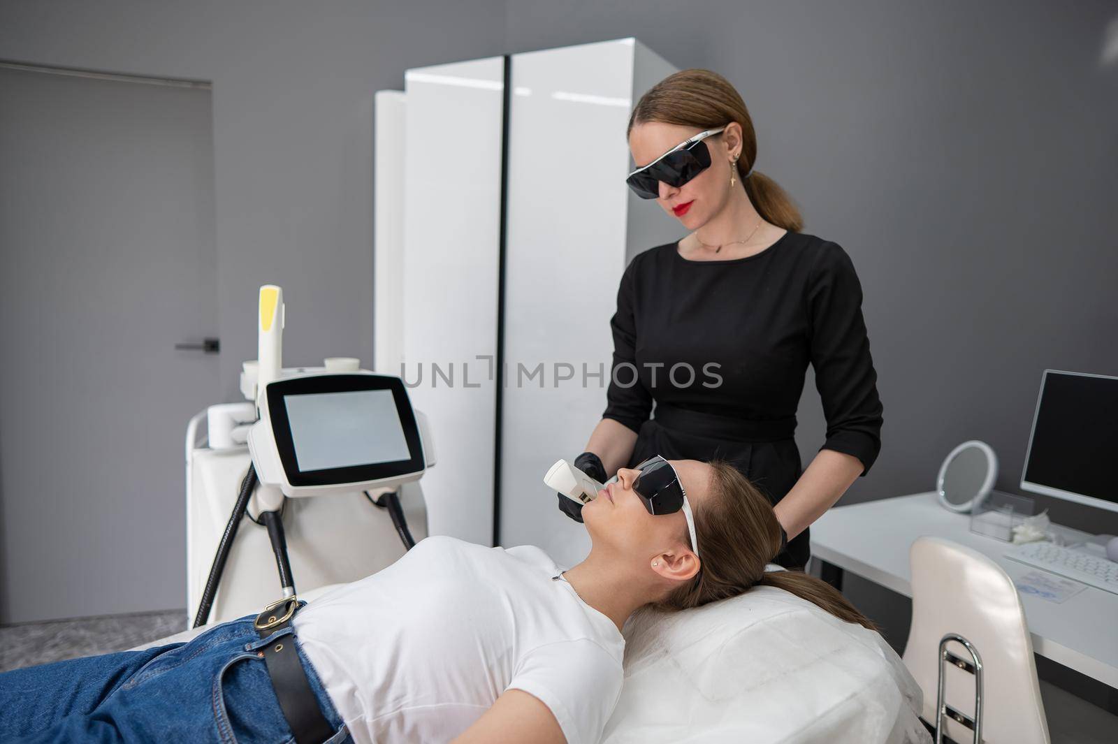 Young caucasian woman in goggles on photorejuvenation procedure. Doctor cosmetologist with a female patient