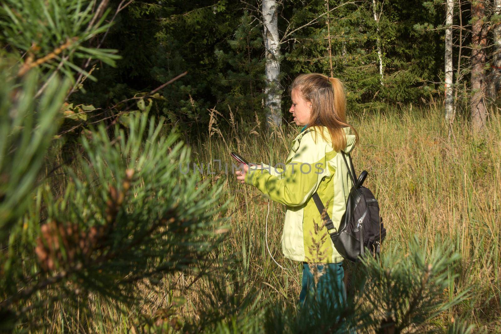 A woman is looking at her mobile phone in the forest. Playing geocaching.