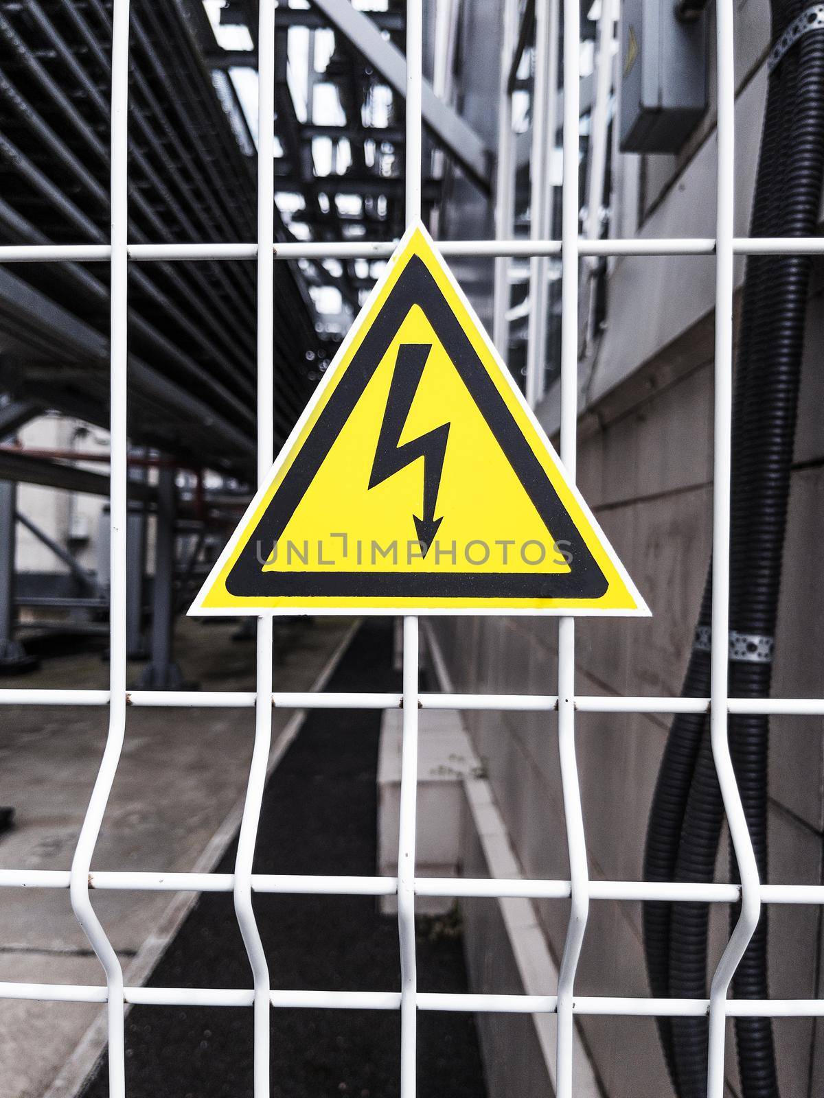 Danger Sign High voltage in the yellow triangle on the metal fence of the grid