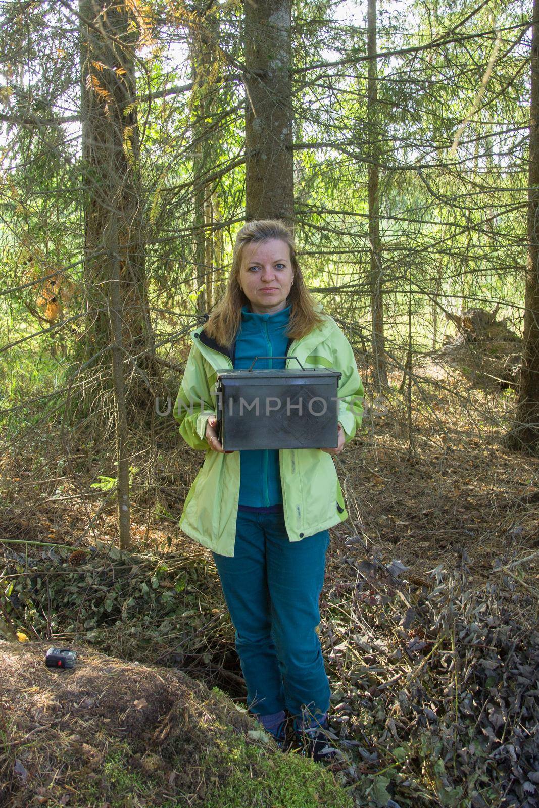 Woman find big metal box. Geocaching in the woods