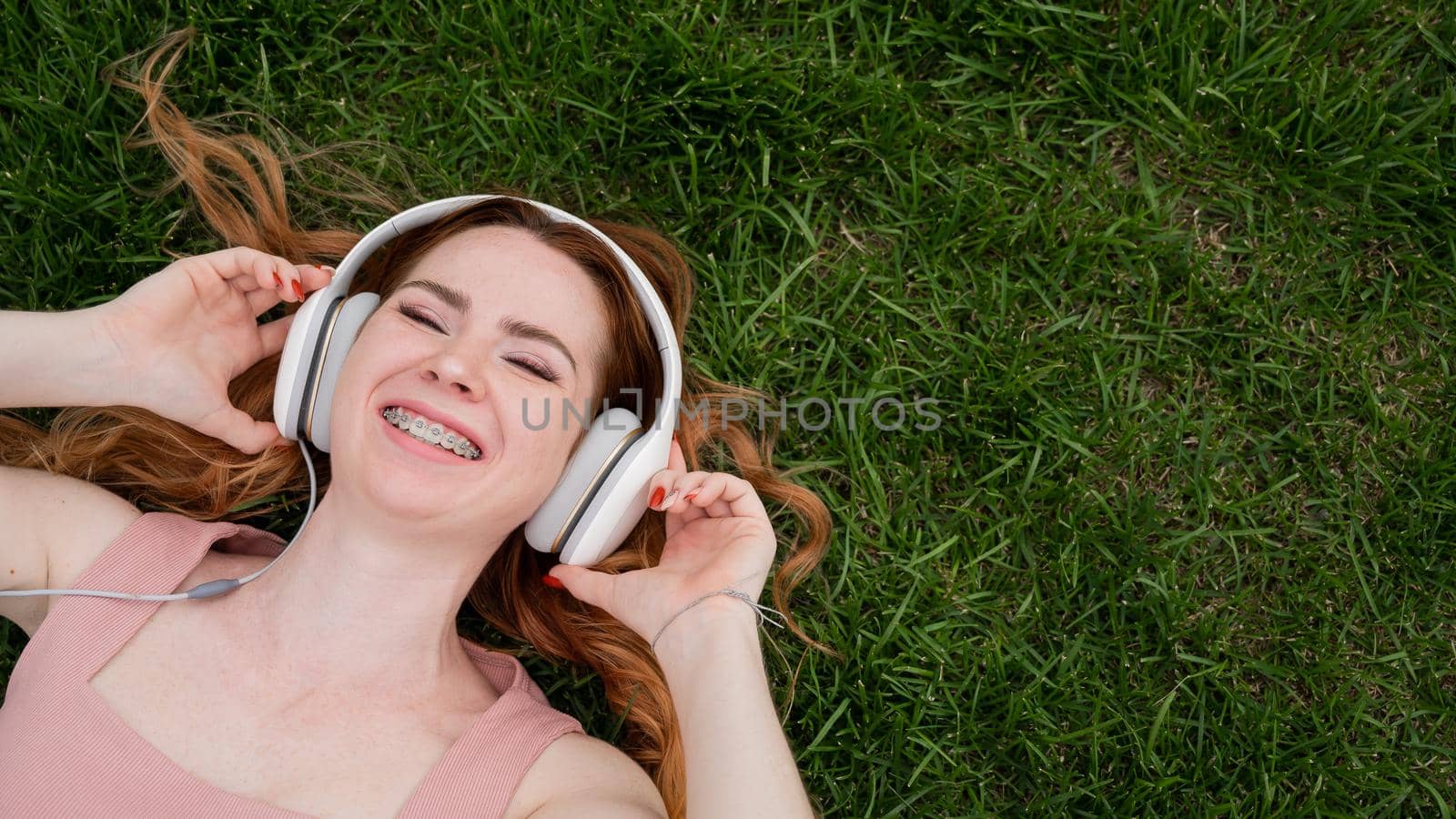 A young red-haired woman lies on the grass and listens to music