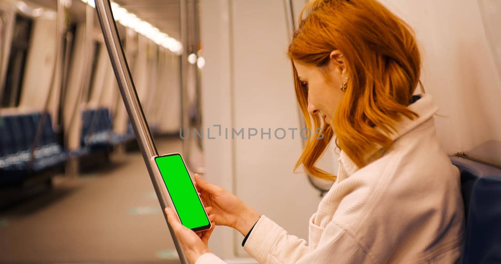 Tourist woman sitting down in a metro and scroll the green screen phone on the train. Using green screen smartphone for advertisement. Lifestyle and transportation concept. Passenger in subway.