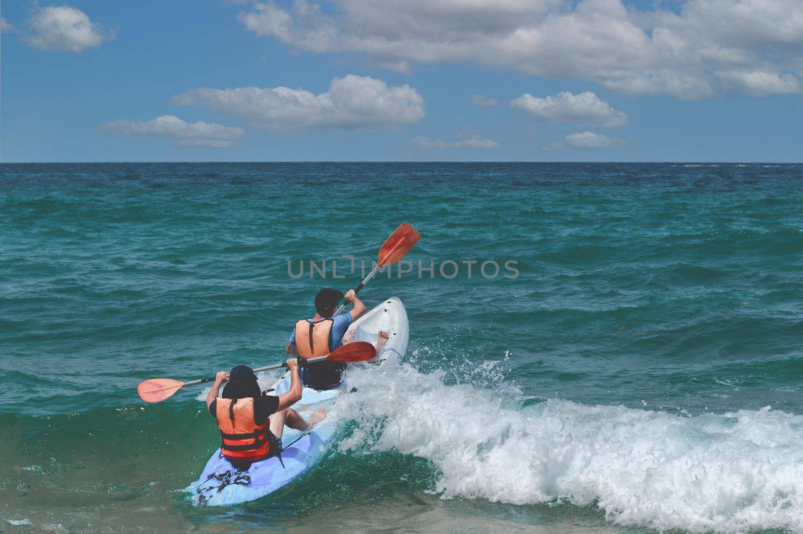 Two kayakers are trying to pass a large coastal wave and swim out into the open sea.