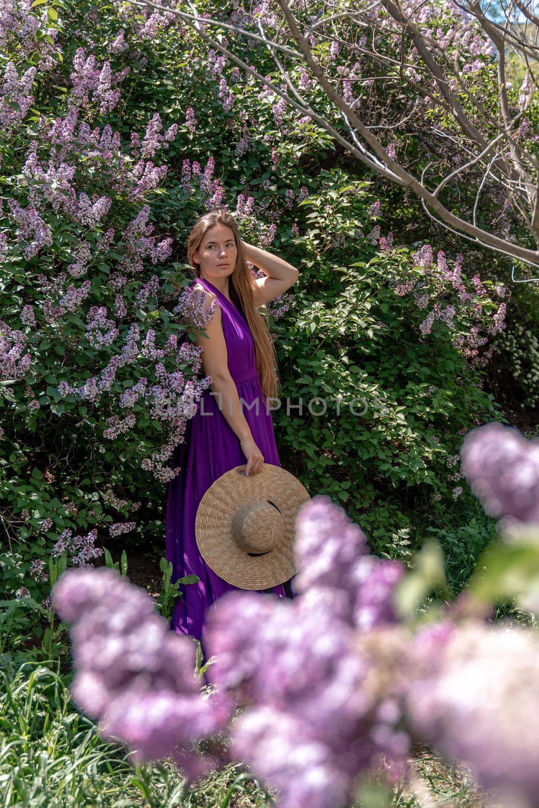 Fashion Model in Lilac Flowers, Young Woman in Beautiful Long Dress Waving on Wind, Outdoor Beauty Portrait in Blooming Garden.