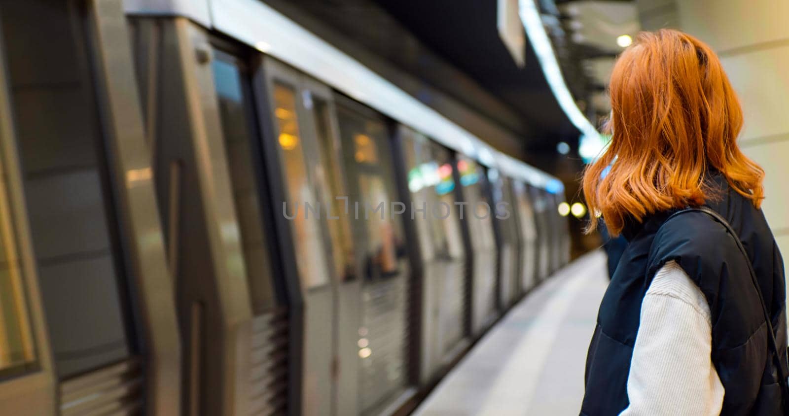 Tourist female waiting at platform of metro station looking at passing train. Busy city people. Urban transportation concept. Underground train arrives at the station