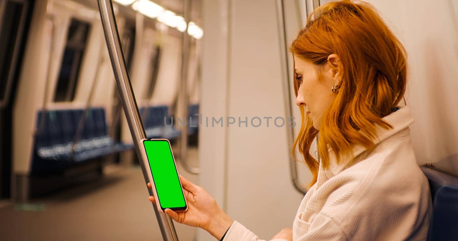 Side view female watching at green screen phone in subway train. by RecCameraStock