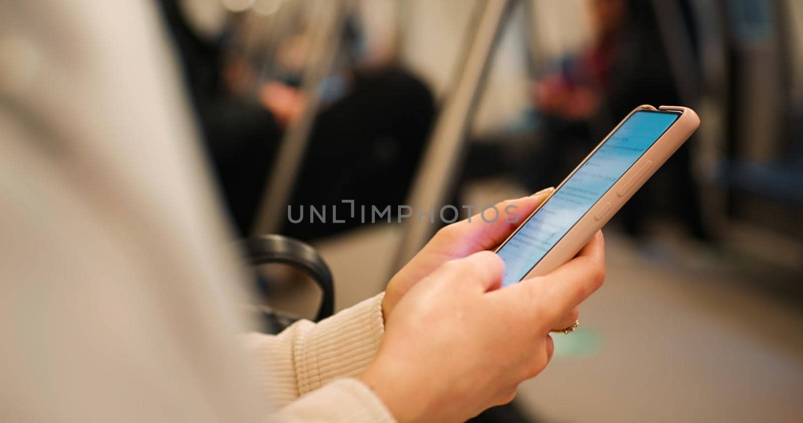 Woman scrolling on the smartphone sitting on a crowded train. Female hands using a gadget in public transport. Technology concept.