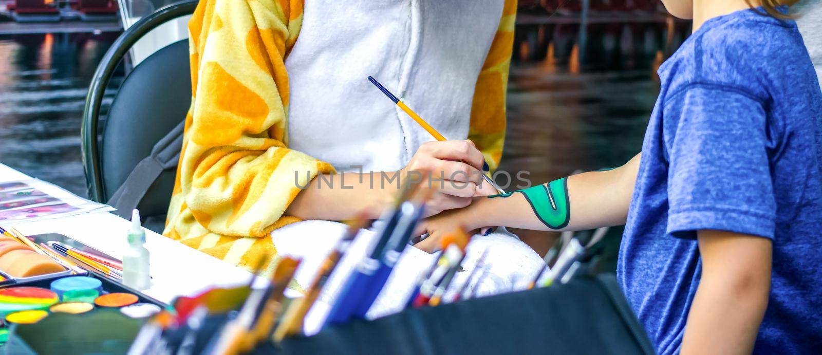 Young girl artist draws a dragon on child's hand. Process of drawing on skin, close-up, banner.