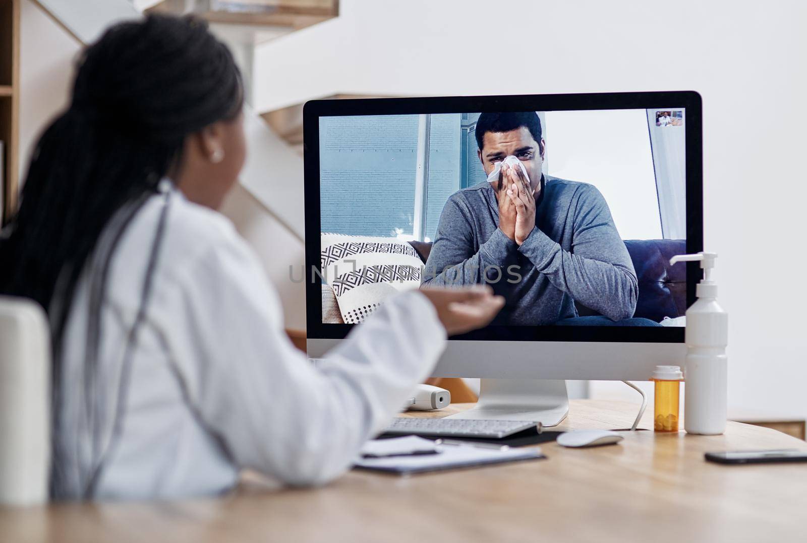 Checking in for a video visit with the doc. a young man blowing his nose during a video call with a doctor on a computer