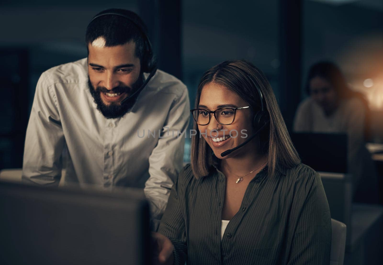 Working the late nights with big smiles on their faces. two call centre agents working together in an office at night. by YuriArcurs